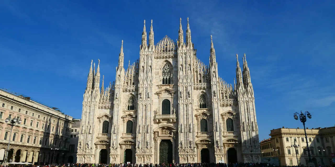 Fachada del Duomo de Milán bajo un cielo azul con turistas en la plaza